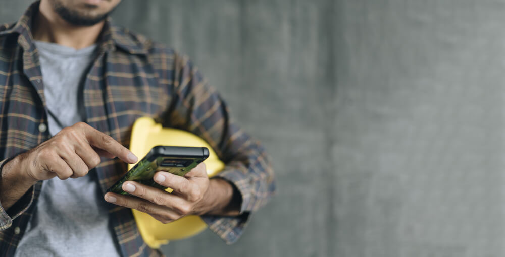 Un artisan sur un chantier, smartphone à la main, symbole de la digitalisation du secteur du BTP.